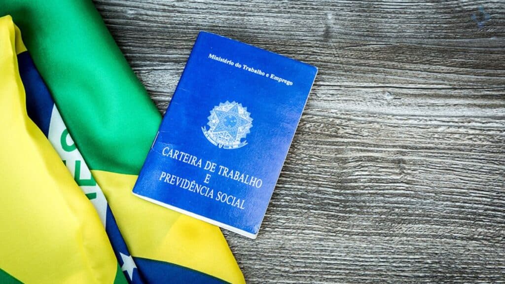 Uma imagem que ilustra uma carteira de trabalho ao lado de uma bandeira do Brasil.