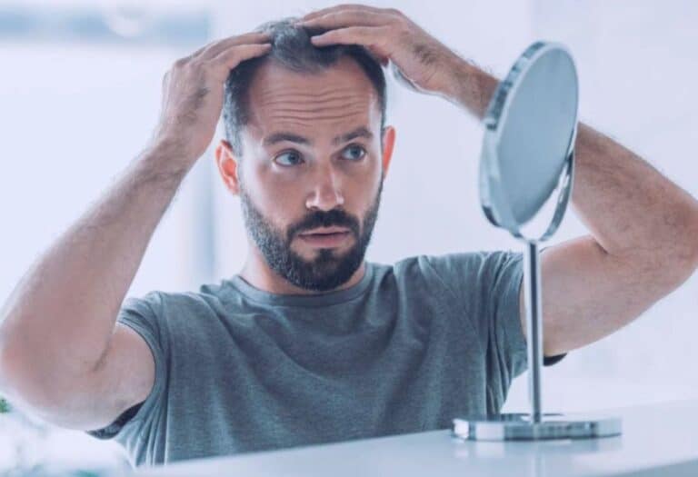 Uma imagem de um home se olhando no espelho com as mãos no cabelo.
